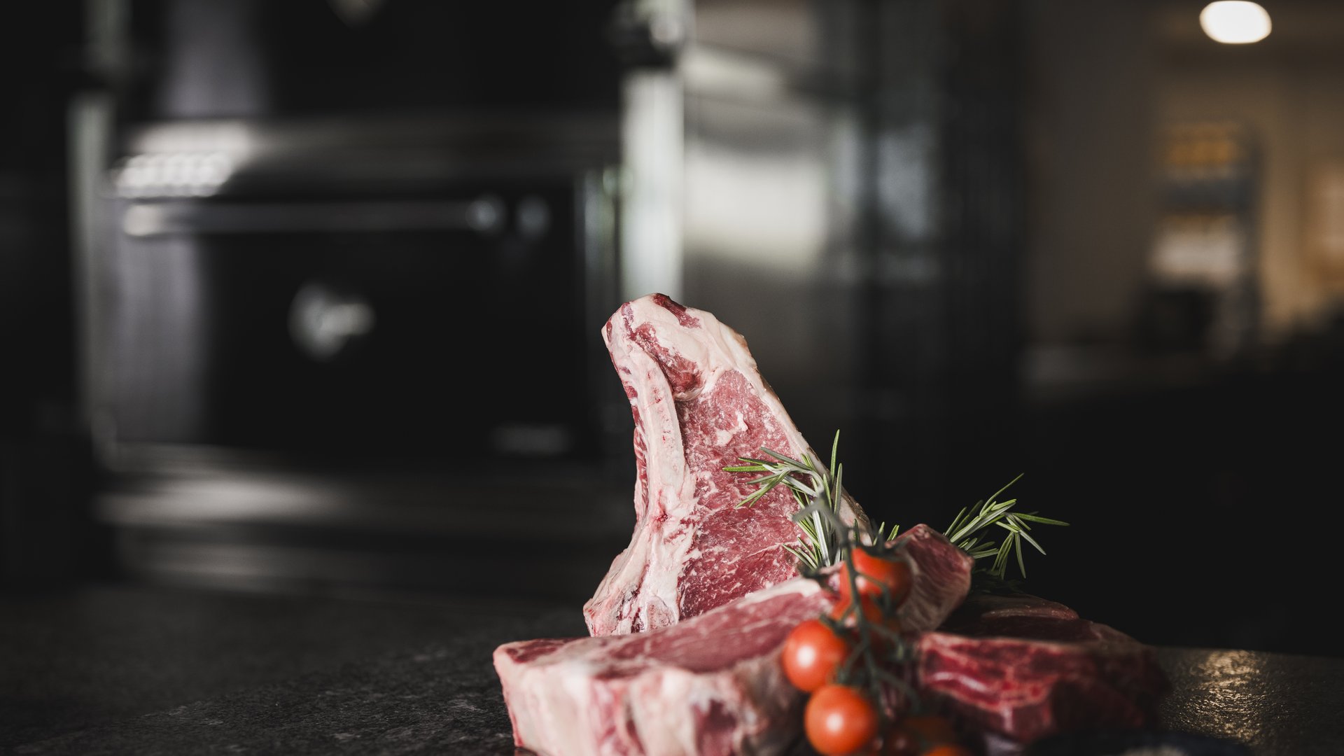 Bistecca cruda con pomodori ciliegia e rosmarino su sfondo scuro