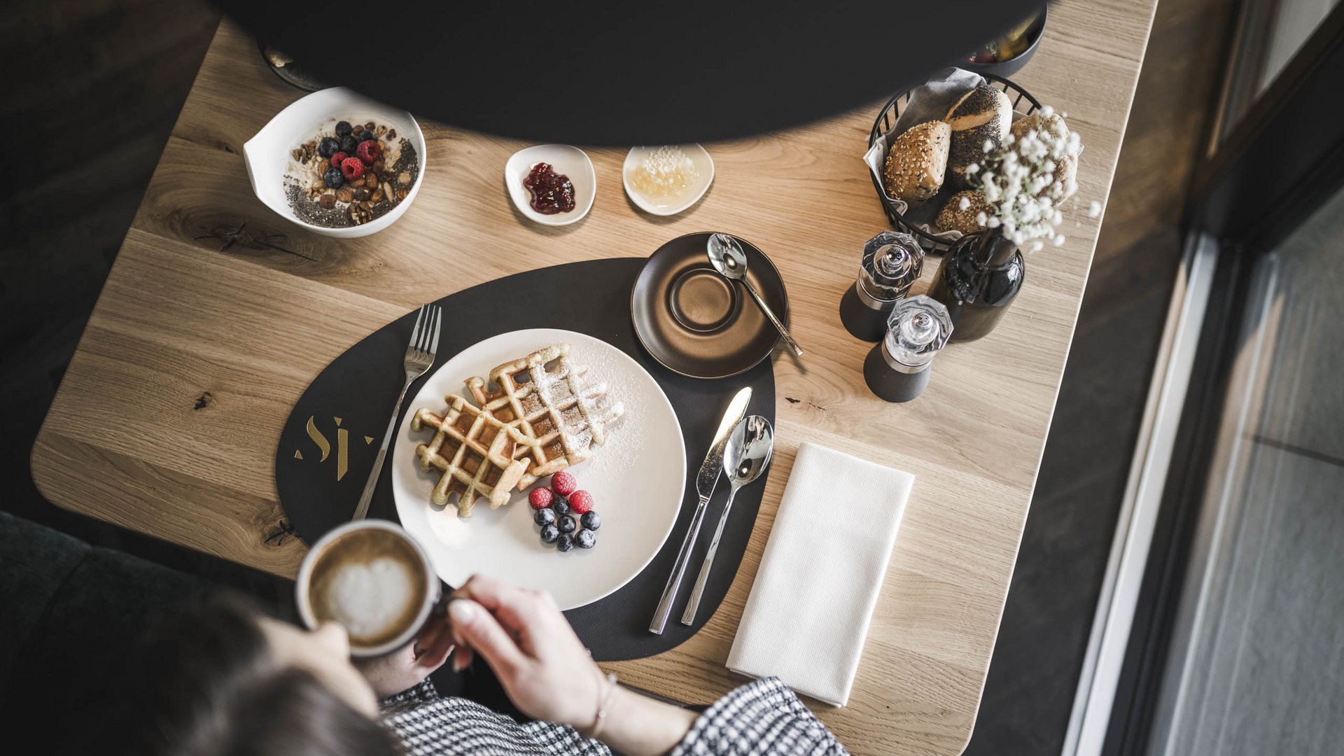 Das wohl schönste Hotel in Dorf Tirol Person trinkt Kaffee an Tisch mit Waffeln, Beeren, Brötchen und Müsli