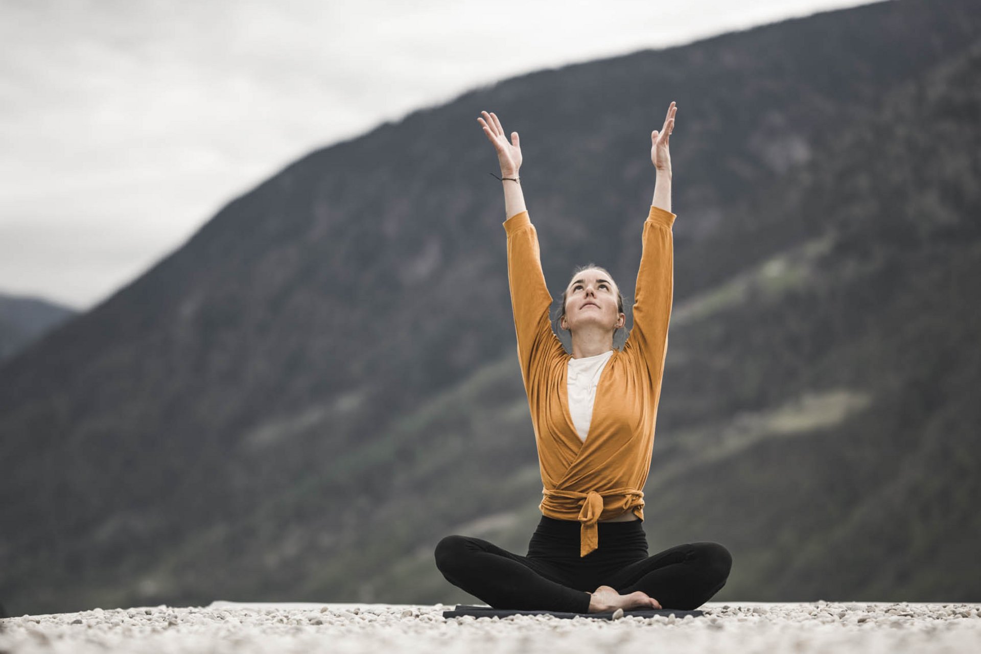 Bewusste Auszeit: Ihr Yoga-Hotel in Meran Frau meditiert im Schneidersitz mit erhobenen Armen vor Bergkulisse