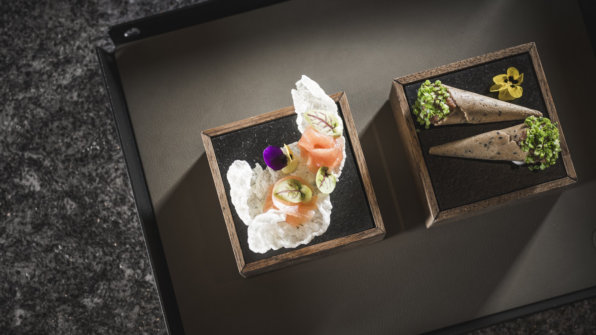 Due antipasti eleganti serviti su piatti neri e cornici di legno