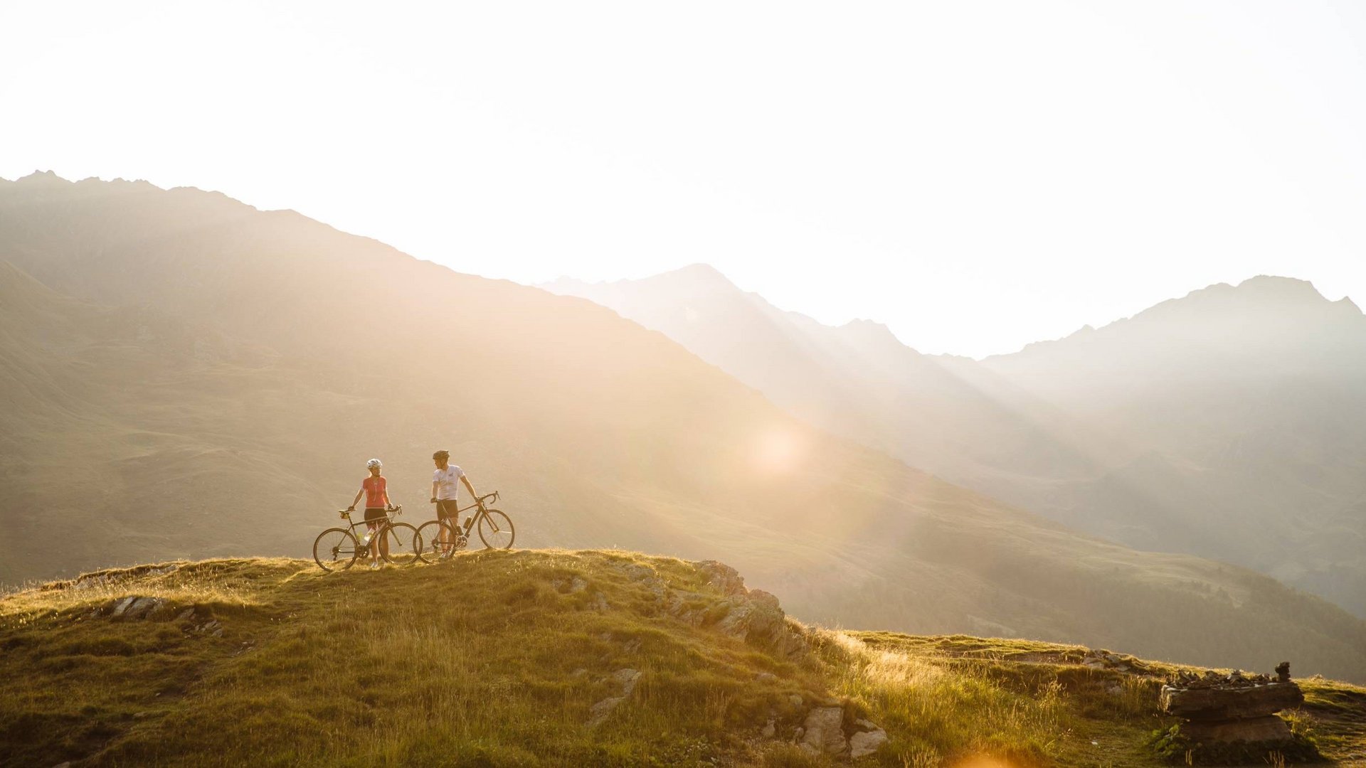 Zwei Radfahrer stehen auf einem Hügel mit Blick auf Sonnenuntergang in den Bergen