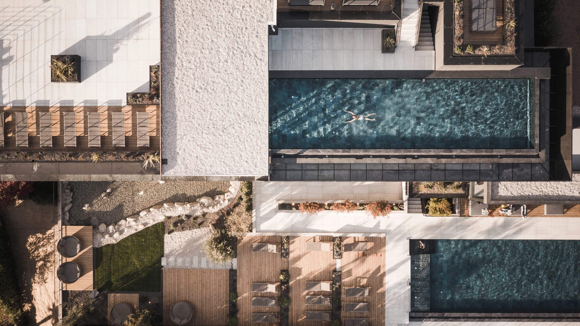 Drohnenansicht eines Pools mit einer Person, umgeben von Liegestühlen und Pflanzen