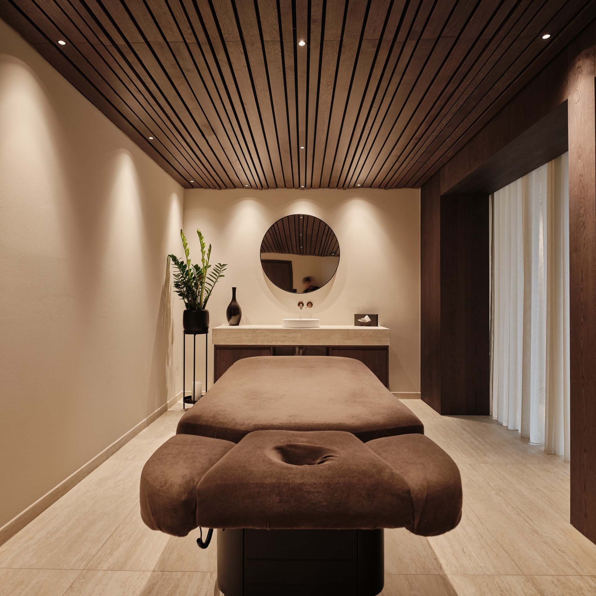 Gemütlicher Massagetisch in modernem Spa-Raum mit Holzdecke und Pflanzen